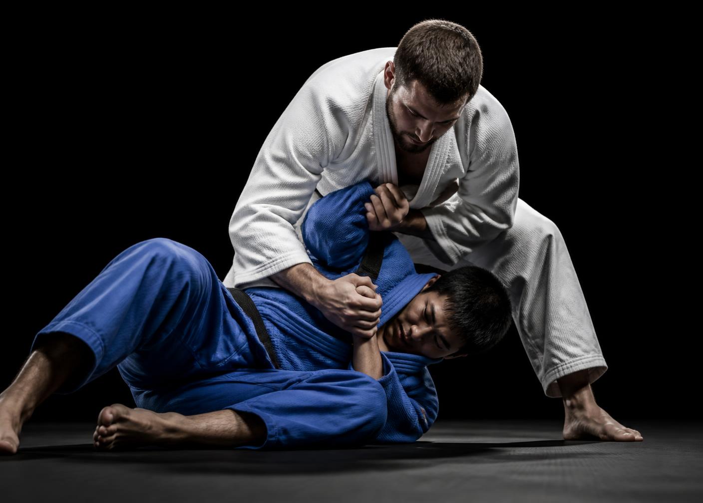 Two competitors grappling on a black tatami competition mat under event lighting